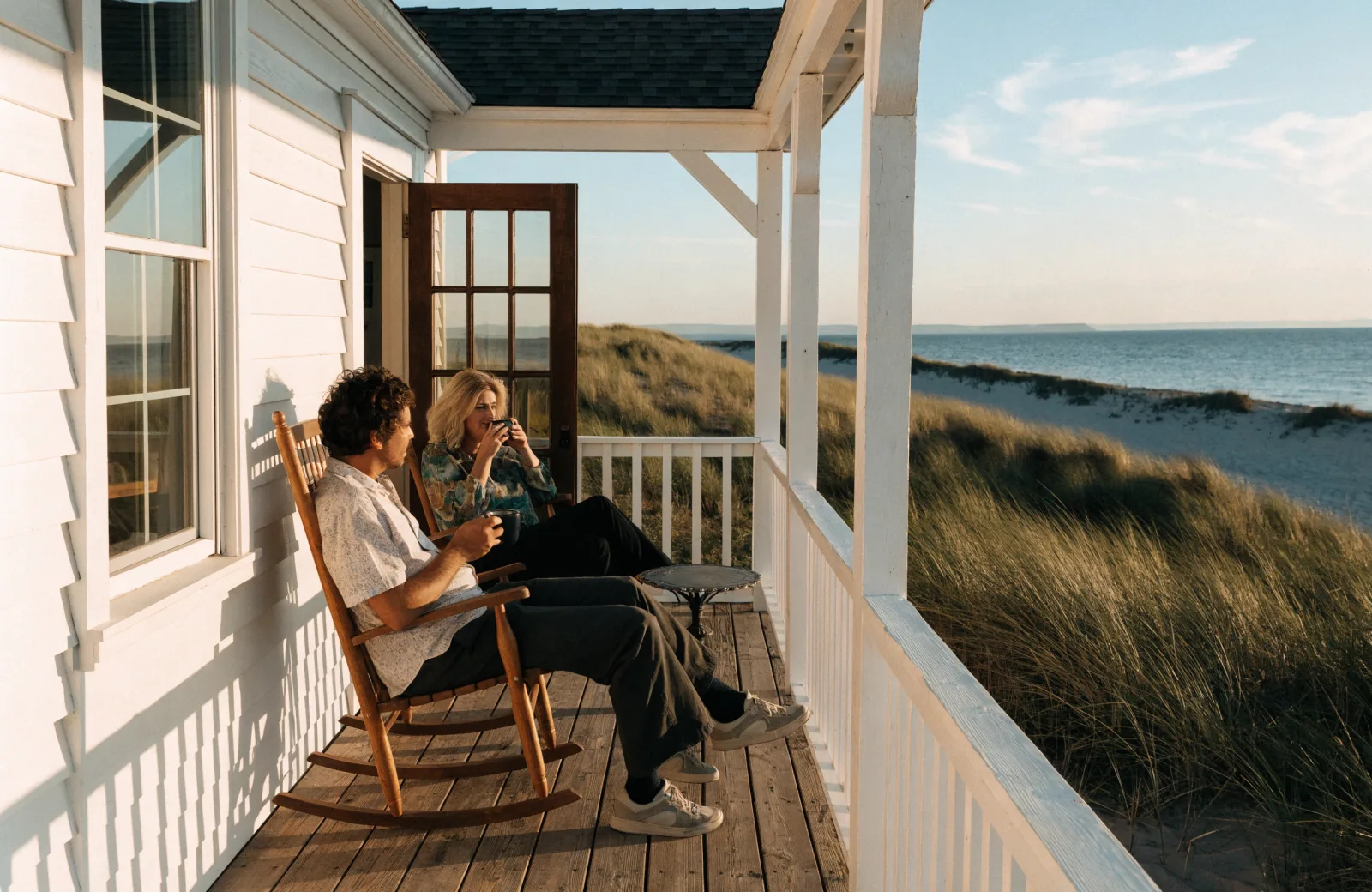Couple with coffee on the porch of a white beach cottage at sunrise on 30A